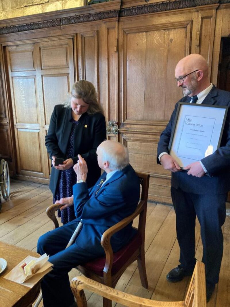 John Avery being presented with his medal by Rachael Maskell and his son, Trevor, holding the citation